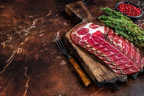 Sliced cured coppa ham on wooden board with thyme. Dark background. Top view Stock Photos