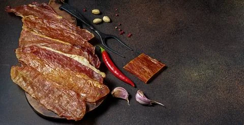 Sliced cured meat on dark background with red chili pepper Fotos de archivo