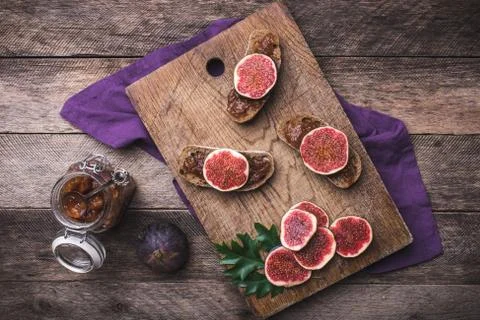 Sliced figs and bread with jam on choppingboard in rustic style Stock Photos