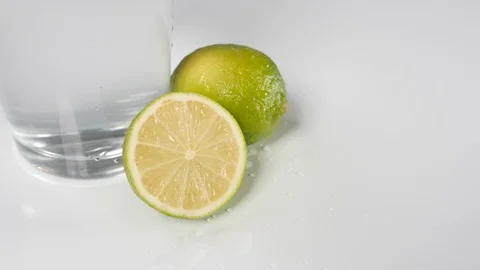 Sliced fresh half lime and whole citrus fruit with water splash dripping Stock Footage 88510192