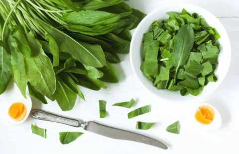 Sliced fresh sorrel leafs with eggs and rustic knife on white table Stock Photos