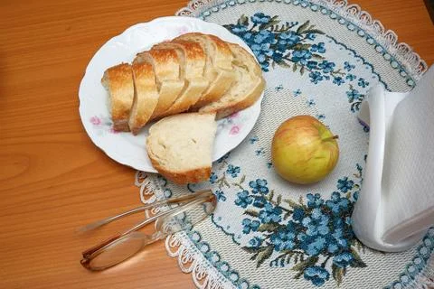 Sliced fresh white bread and a ripe red apple on an embroidered napkin. Stock Photos