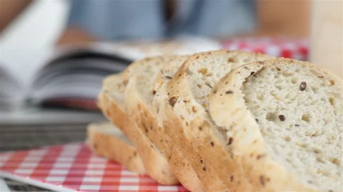 Sliced grain bread and jars with seeds. Woman leafing through cookbook. Stock Footage 100587443