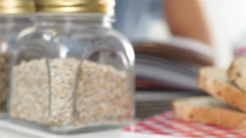 Sliced grain bread and jars with seeds. Woman leafing through cookbook. Stock Footage 100587466