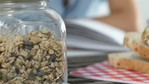 Sliced grain bread and jars with seeds. Woman leafing through cookbook. Video stock 100587494