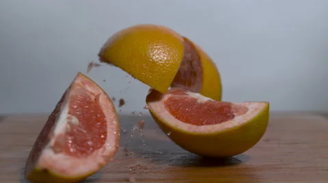 A sliced, grapefruit falls in slow motion onto a cutting board and separates Stock Footage 64562421