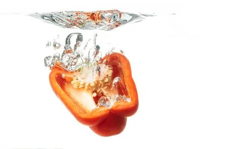 Sliced in half red bell pepper falls to the water, causing bubbles and scatte Stock Photos