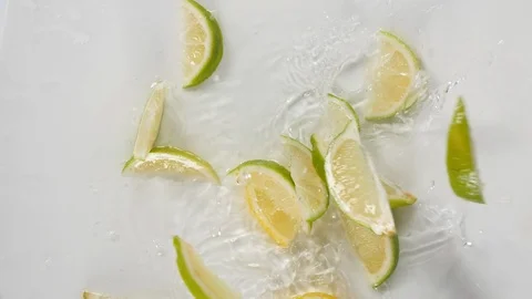 Sliced lime and lemon fruit dropped from above onto white background Stock Footage 88509604