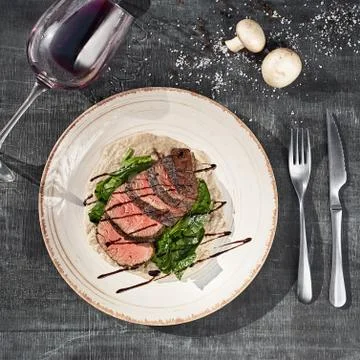 Sliced medium rare grilled beef steak with mushroom sauce and greens on a pla Stock Photos