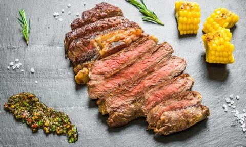 Sliced medium rib eye beef steak meat with chimichurri on black background Stock Photos
