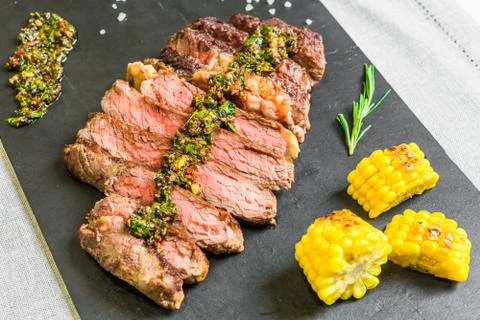 Sliced medium rib eye beef steak meat with chimichurri on black background Stock Photos