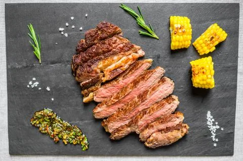 Sliced medium rib eye beef steak meat with chimichurri on black background Stock Photos