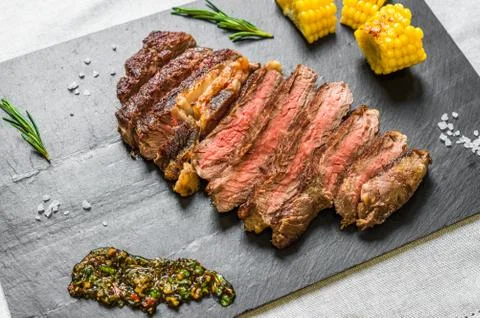 Sliced medium rib eye beef steak meat with chimichurri on black background Stock Photos