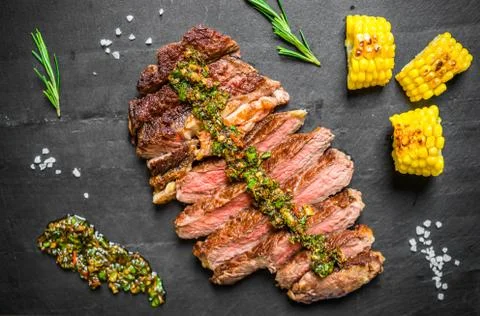 Sliced medium rib eye beef steak meat with chimichurri on black background Stock Photos