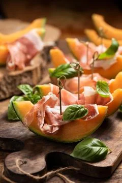 Sliced melon with ham and basil leaves, served on a wood chopping board Stock Photos