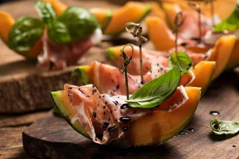 Sliced melon with ham and basil leaves, served on a wood chopping board Foto stock