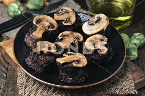Sliced mushrooms and blood sausage, fried in a porcelain dish on wood Stock Photos