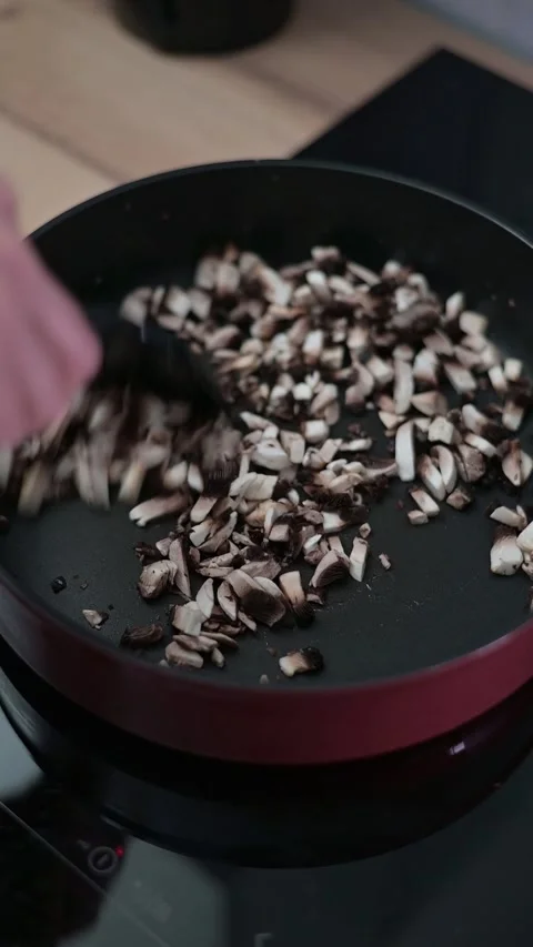 Sliced mushrooms are being cooked in a pan, with hands using a spatula to stir Stock-Footage 337112246