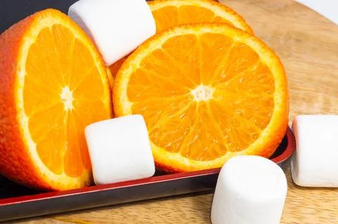 A sliced orange and white marshmallows lie on a wooden board. Stock Photos
