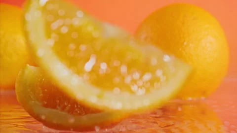 Sliced orange falls into the water on an orange background at super slow motion  Stock Footage 338064696