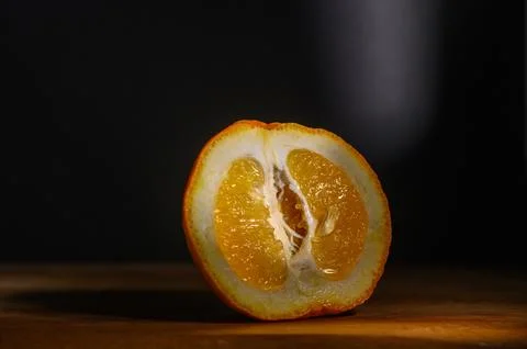 Sliced orange reveals vibrant sections under dramatic lighting in a dark se.. Stock Photos
