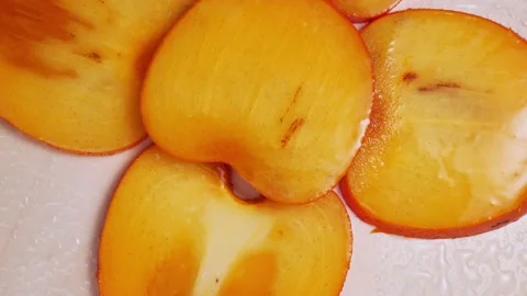 Sliced persimmon close-up rotates under drops of water Stock Footage 147081521