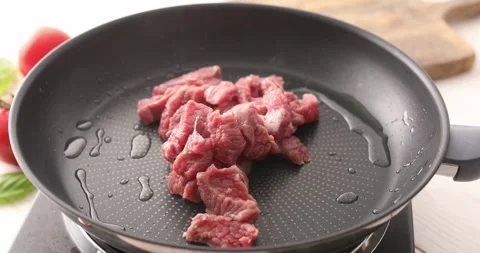 Sliced pieces of raw meat are placed in a frying pan. Stock Footage 250020150