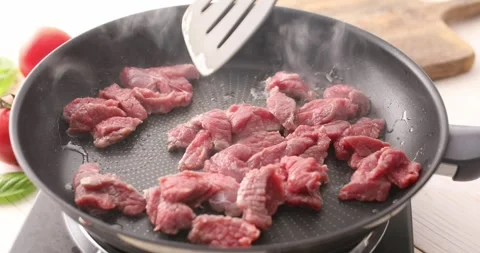 Sliced pieces of raw meat are mixed with a spatula in a frying pan. Stock Footage 250020506