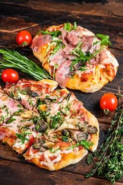Sliced pizza with prosciutto parma ham, arugula and parmesan cheese. Dark wooden Stock Photos