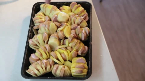 Sliced potatoes with sausages on a baking sheet are sprinkled with spices. Stock Footage 160963827