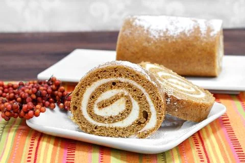 Sliced pumpkin roll cake with whole cake in background. Fall setting and co.. Stock Photos
