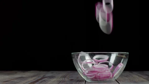 Sliced purple onion falls down into empty glass bowl on a wooden table Stock Footage 129745719