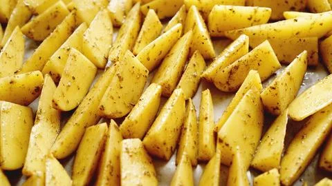 Sliced raw potatoes on a baking sheet with spices and rosemary, top view Stock Photos