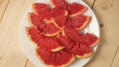 Sliced red grapefruit rotating on a white plate Stock Footage 341822915
