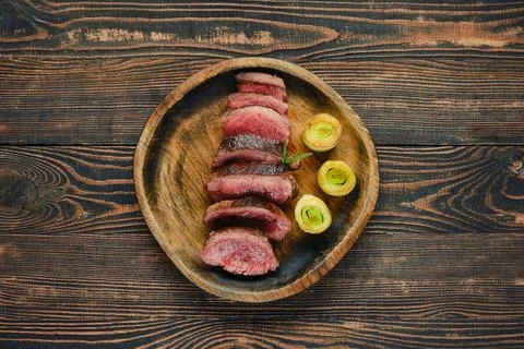 Sliced roast beef steak with roasted leek served on a wooden plate against .. Foto stock