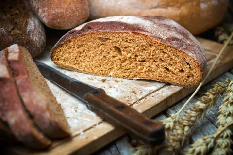 Sliced rye round bread and wheat ears witha knife on the old wooden table Foto stock