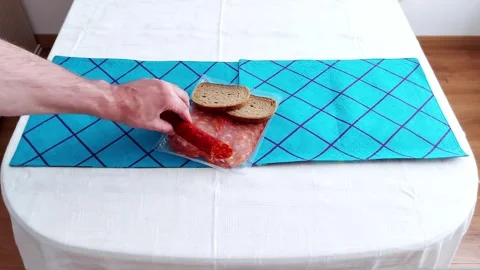 Sliced Sausage and Rye Bread on Blue Cloth: A Simple Table Ritual Stock Footage 314818259