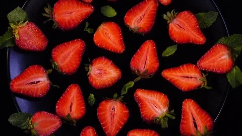 Sliced strawberry with mint leaves on the black plate. Closeup rotation 4K Stock Footage