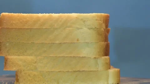 Sliced toasted white bread stack rotating on blue background, wooden slicing boa Stock Footage 254126909