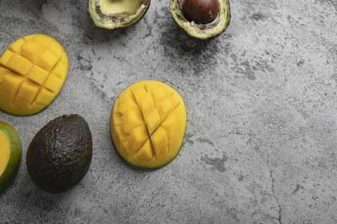 Sliced tropical fruit mango and broken avocado on marble surface Stock Photos
