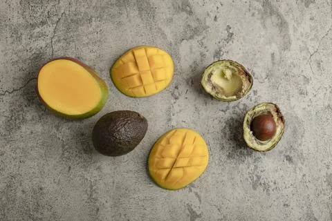 Sliced tropical fruit mango and broken avocado on marble surface Stock Photos