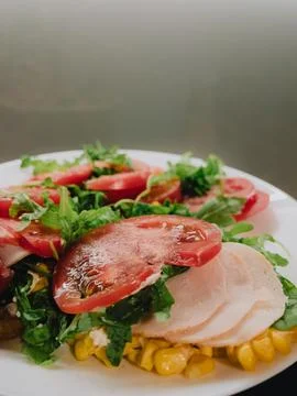 Sliced turkey breast, corn kernels, tomato slices and fresh arugula create Foto stock
