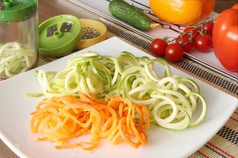 Sliced vegetables and container of vegetable slicer on kitchen table. Stock Photos