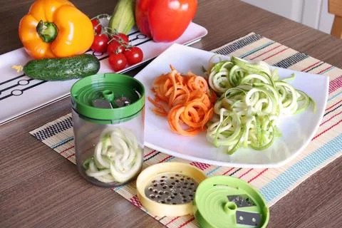 Sliced vegetables and container of vegetable slicer on kitchen table. Stock Photos