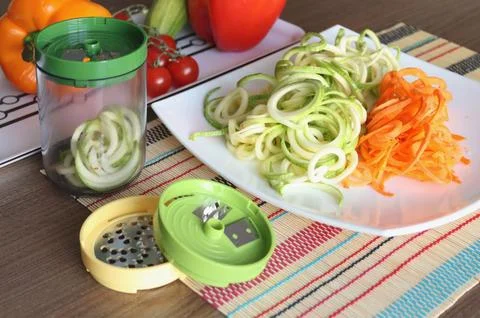Sliced vegetables and container of vegetable slicer on kitchen table. Stock Photos