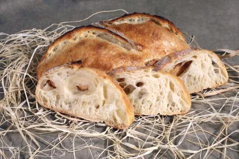 Sliced white bread lying in straw on grey linen tablecloth Stock Photos