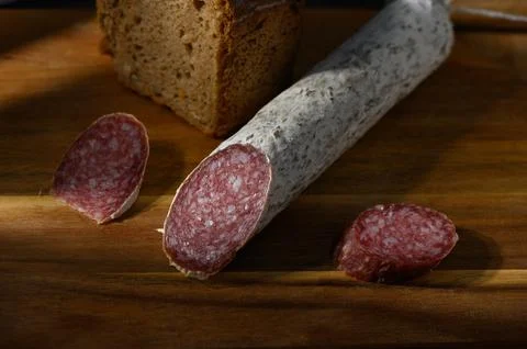 Slices of artisanal salami with rustic bread on a wooden board in warm light 库存照片