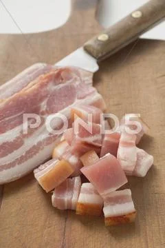 Slices of bacon & diced bacon on chopping board with knife Stock-Fotos