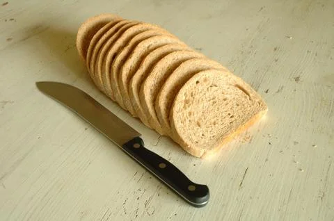 Slices of bread and knife on old wooden table Stock Photos