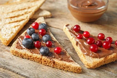 Slices of bread with chocolate paste and berries on wooden table Stock Photos